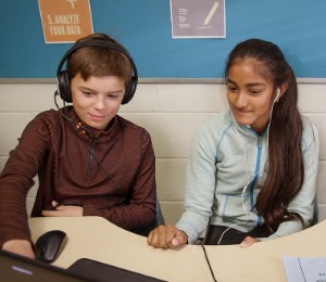 Two students working on a computer with headphones in