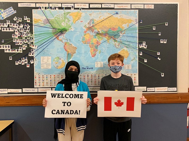 Picture of a student holding a piece of paper that reads Welcome To Canada and another student holding a picture of the Canadian Flag