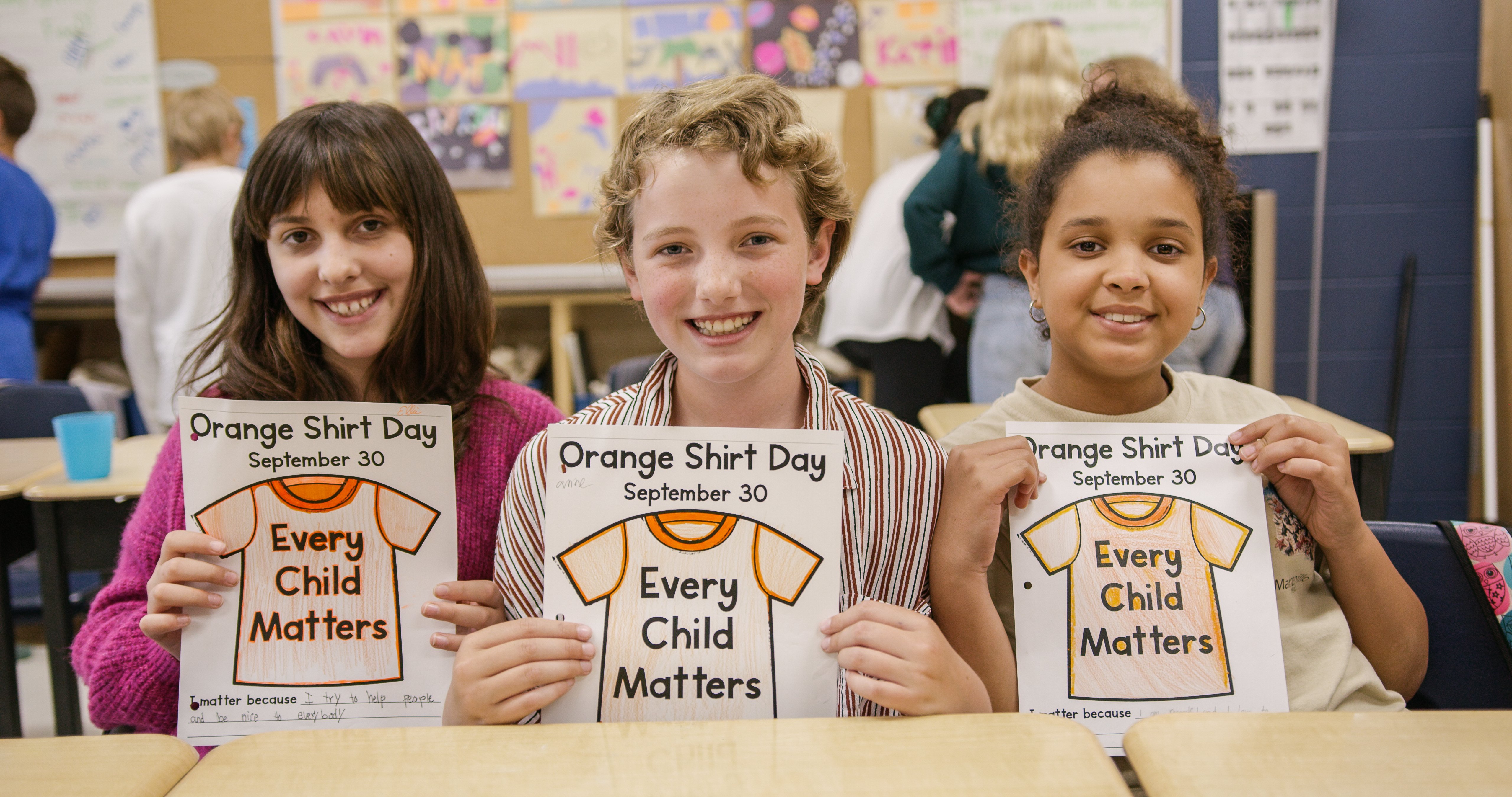 Three students holding up Orange Shirt Day artwork 