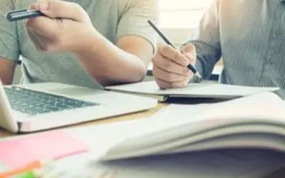 one person writing in a notebook and one person working on a laptop