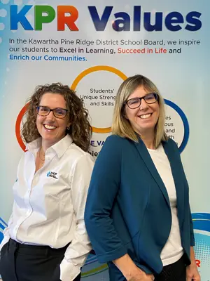 2 women standing in front of a KPR Values banner